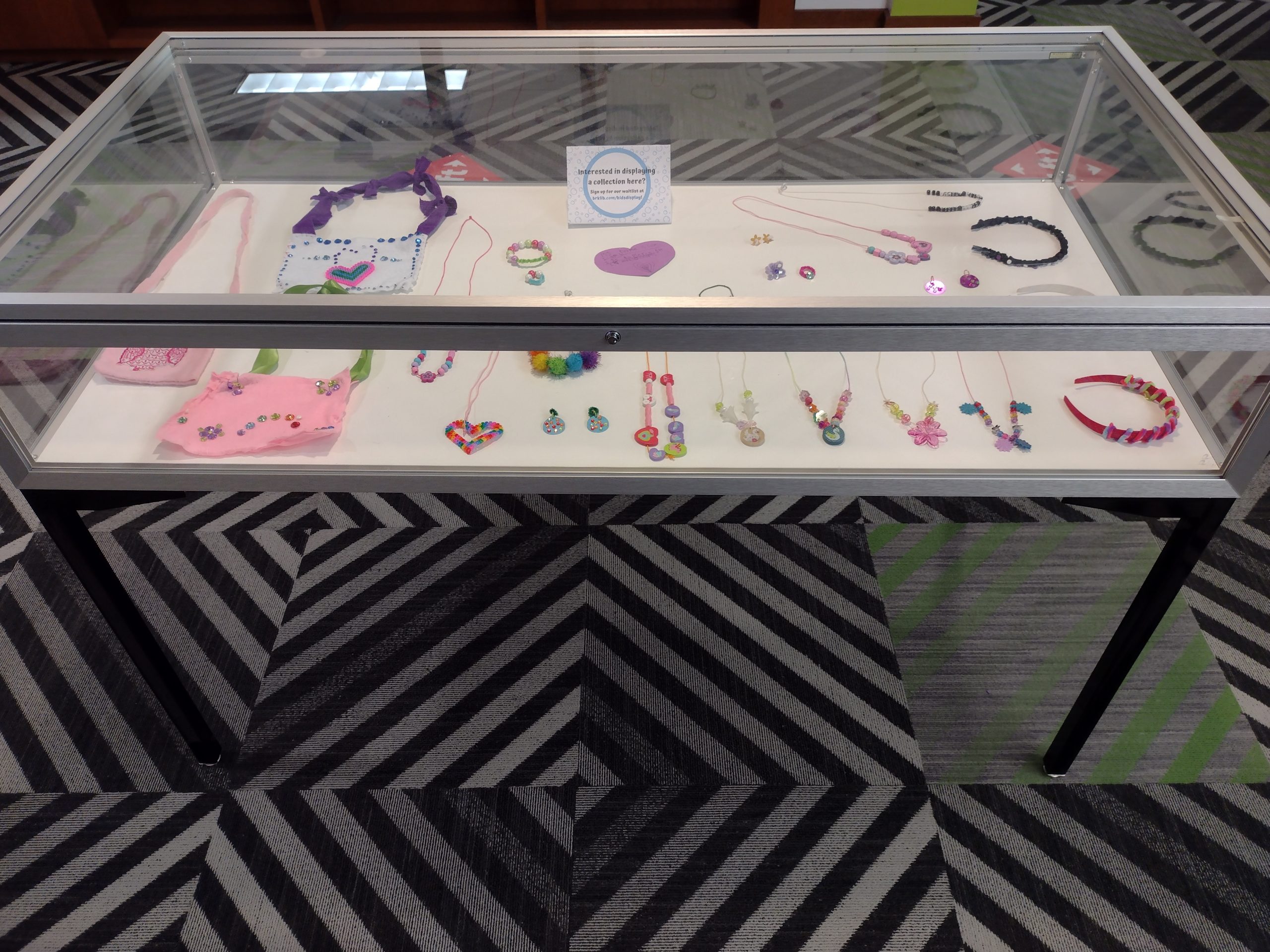 Display case filled with pink and purple plastic jewelry made by six year old Lille