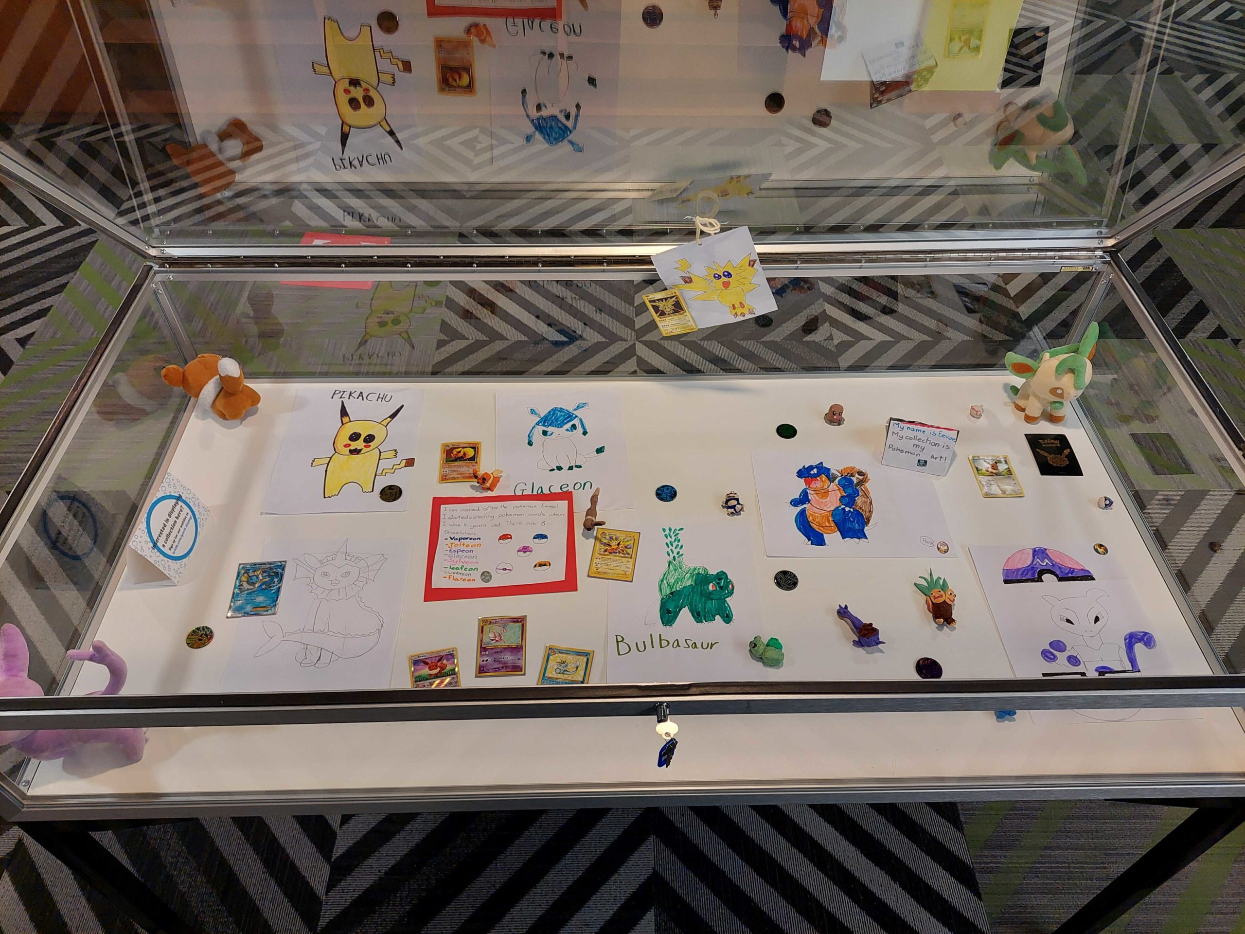 display case filled with pokemon art, figures, and cards