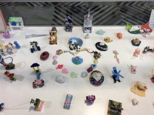 Display case of craft projects, including painted shells, LEGO sculptures, and Model Magic
