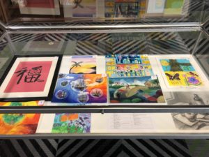 Display case of artwork from Global Youth Philanthropy Art Exhibition 2022 including painting, drawing, and calligraphy