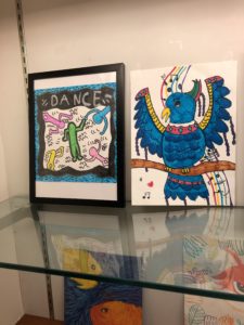 Display case of artwork, including a blue bird and a Keith Haring-inspired drawing