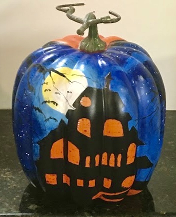A pumpkin painting with a haunted house, dark blue sky, large yellow moon, and bats flying.