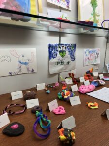 Close-up of drawings, clay, and pipe-cleaner art in a display case
