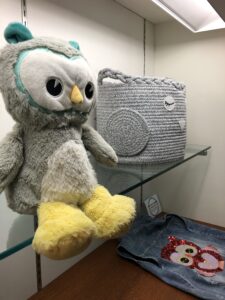Close-up of stuffed animal owl, owl-shaped basket, and a sequined owl on a jean jacket