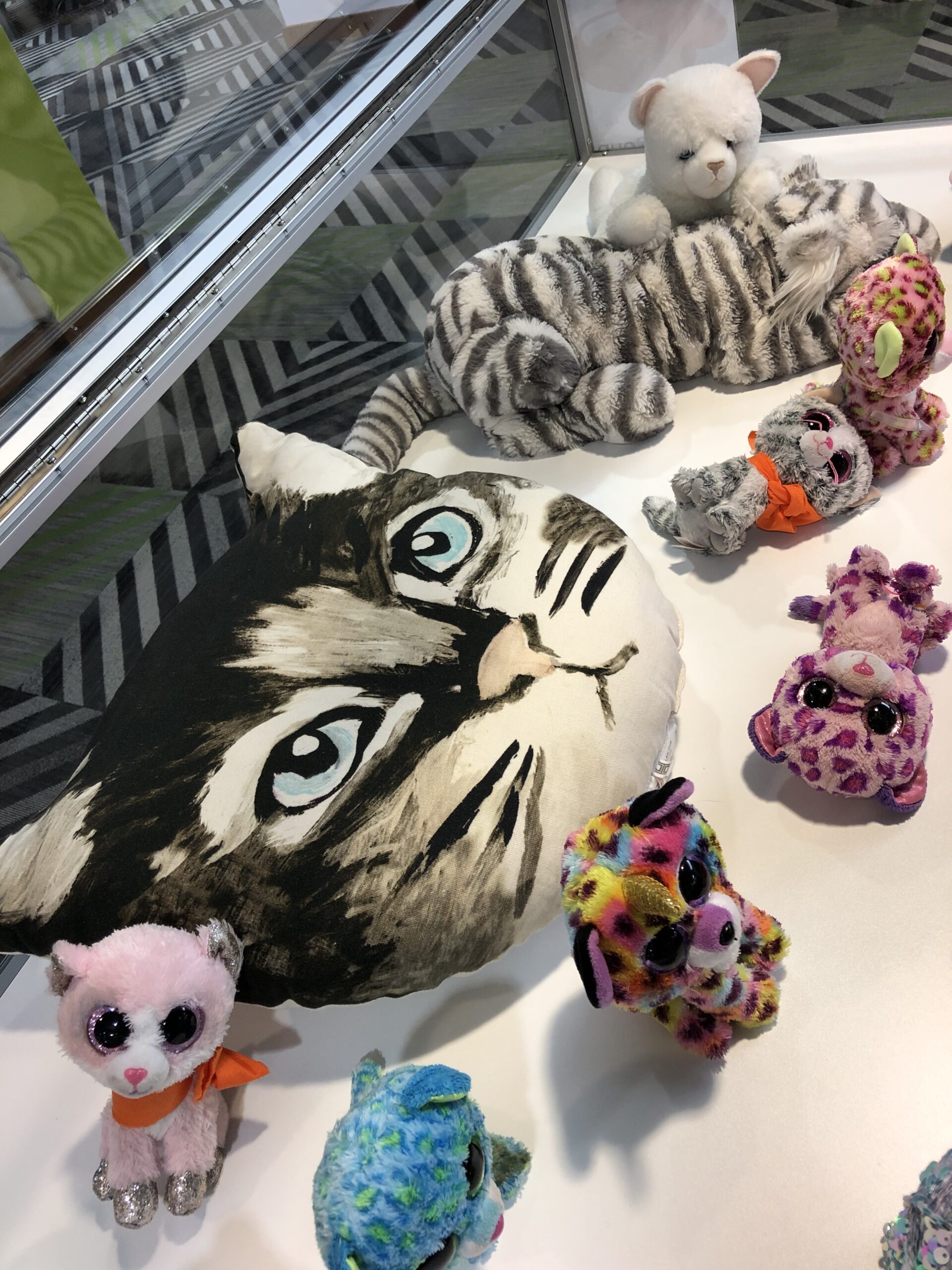 Display case with collection of cat stuffed animals and a cat-shaped pillow