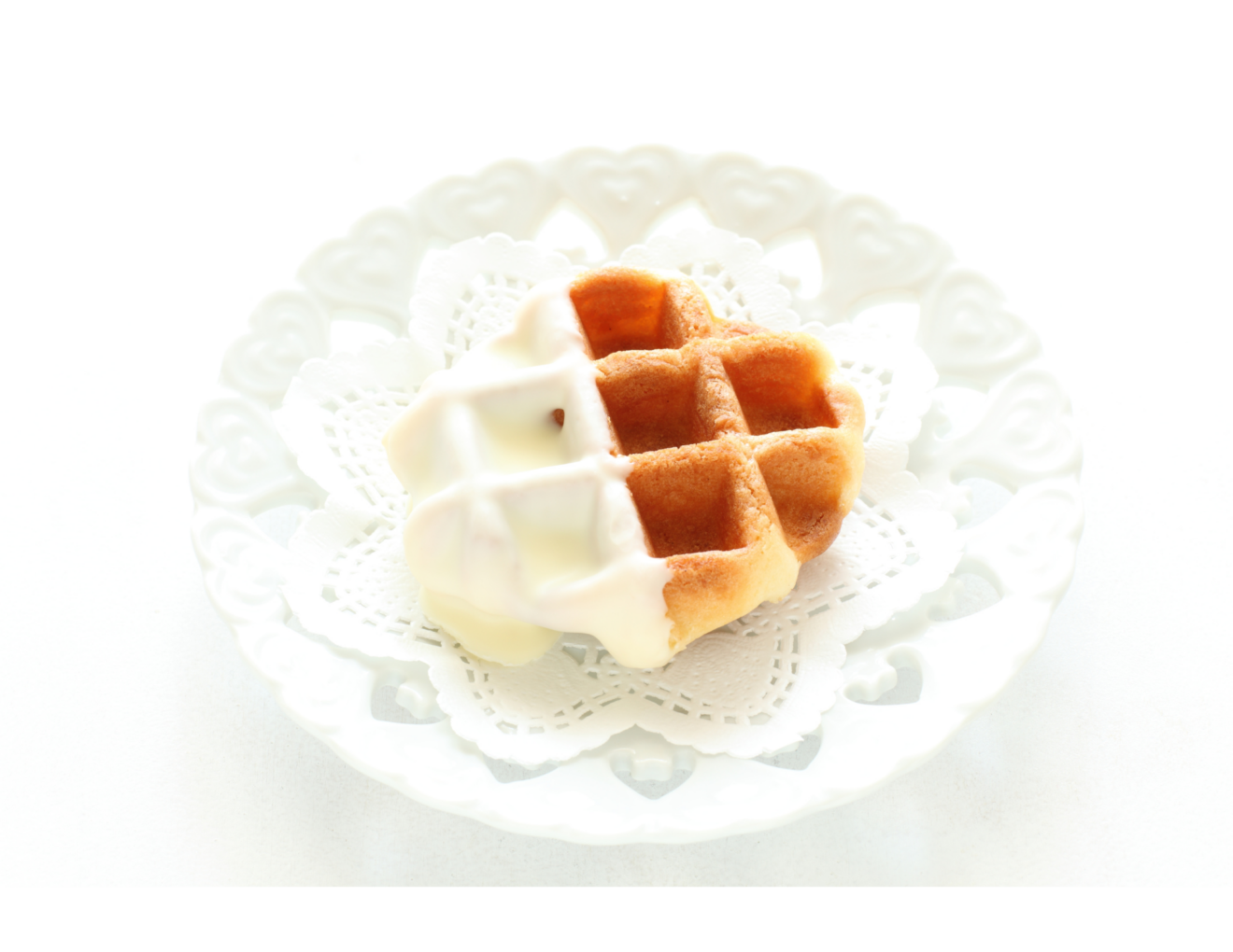 A waffle half covered in white chocolate on a white plate decorated with a white doily.