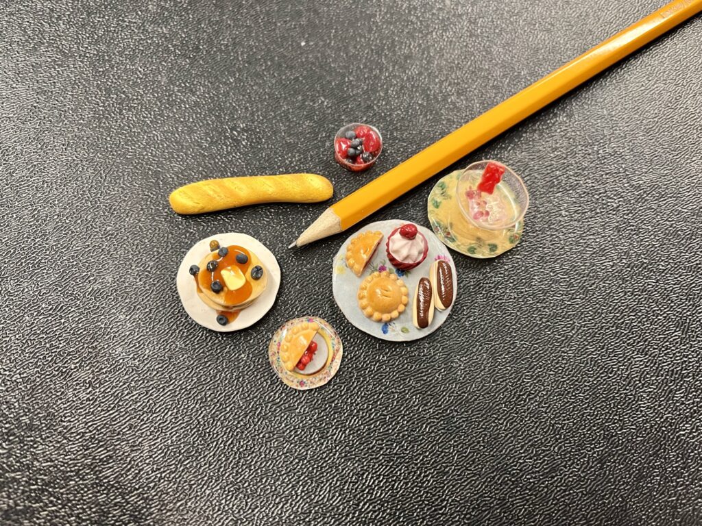 Tiny food made of polymer clay on a black background with a pencil to show a size comparison.