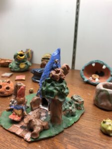 A treehouse, bird, and gnome made of clay in a display case