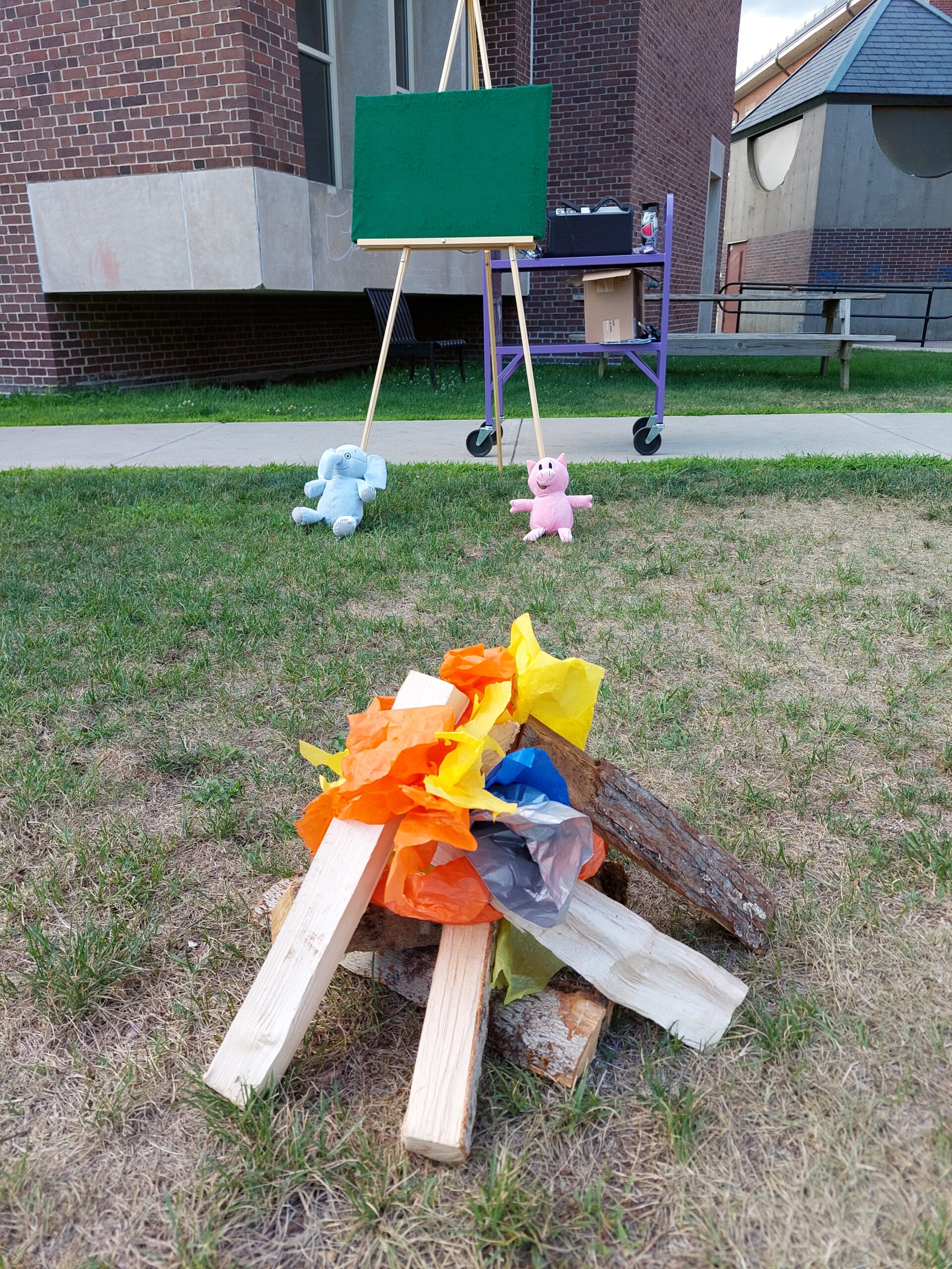 pile of logs made to look like a campfire with tissue paper, on a grassy lawn, set up for a storytime