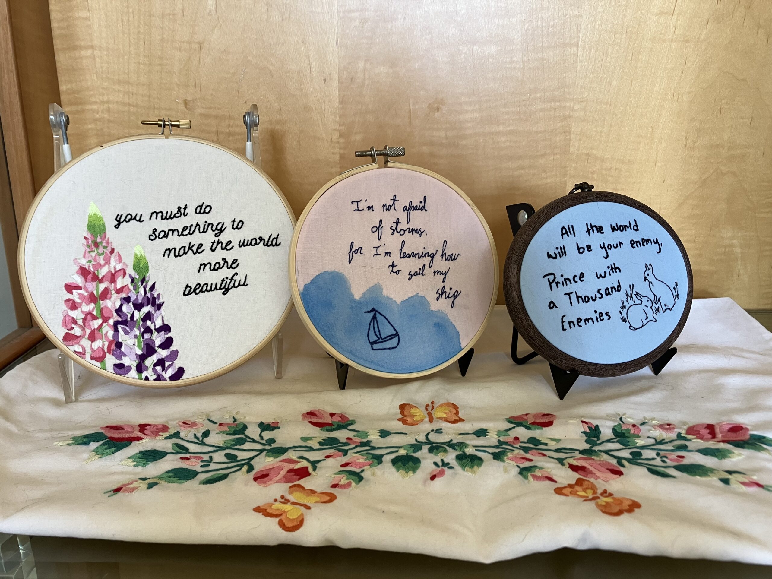 Three pieces of needlework in embroidery hoops, on top of an embroidered pillowcase