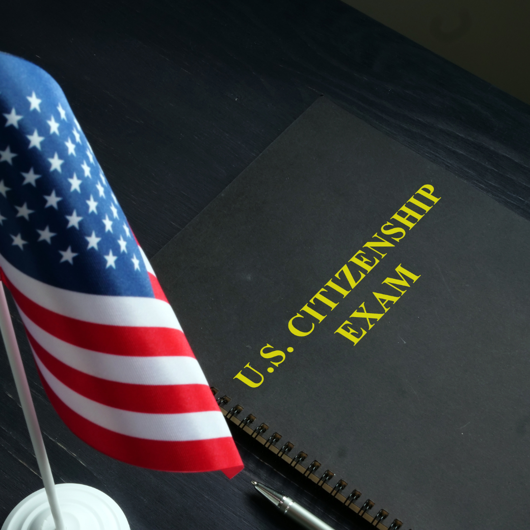 A black book that says U.S. Citizenship Exam, next to a desk-sized American flag