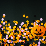 Black, orange, and pink confetti, and two paper jack-o-lanterns on a black background
