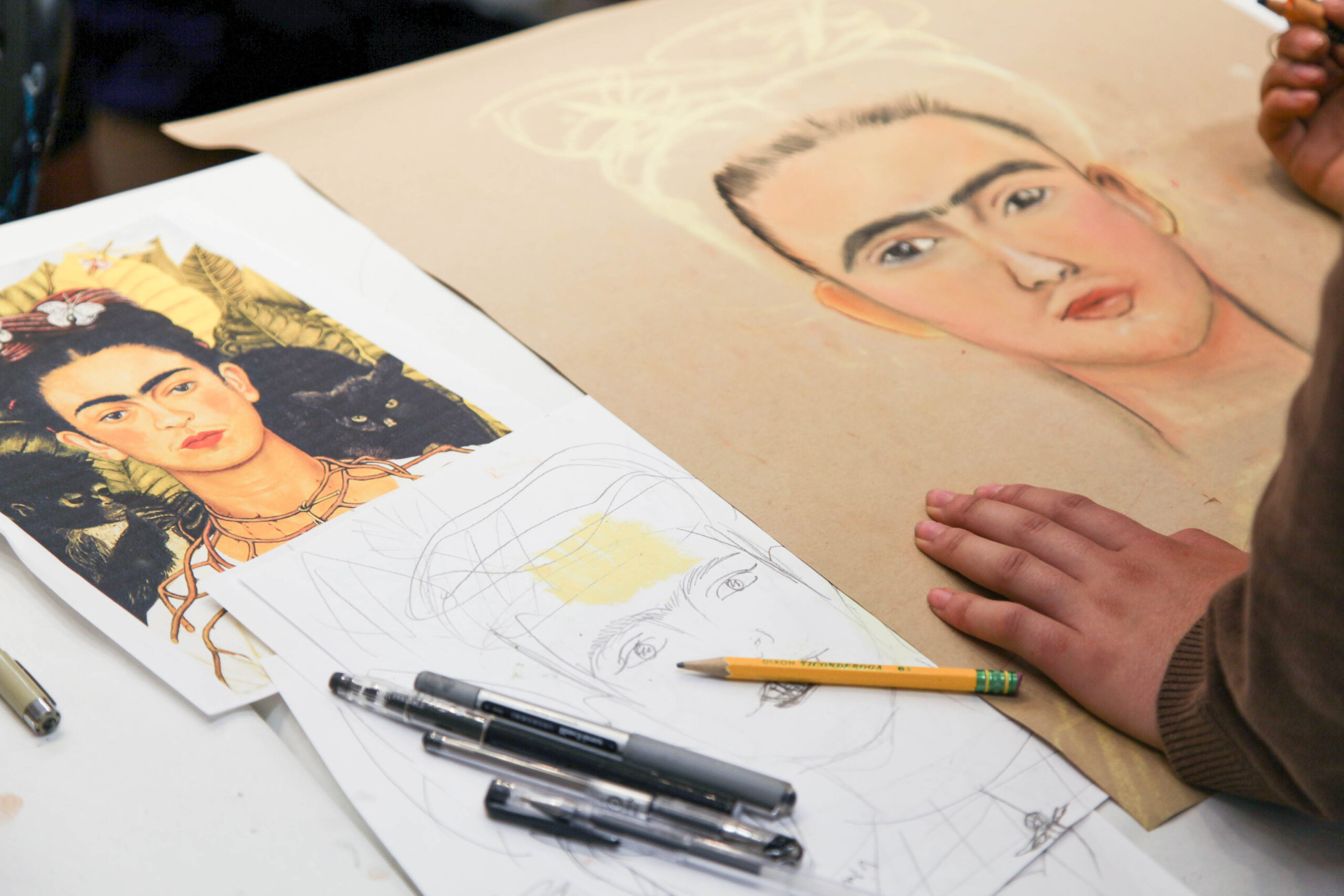 Photo of a sketch and color drawings of Frida Kahlo.