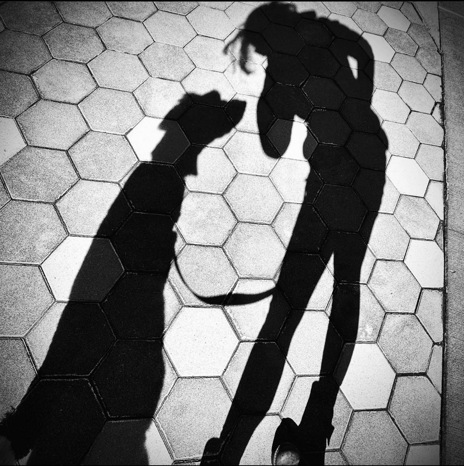 black and white photo of shadows on tiled floor of woman and dog