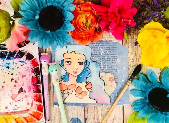 drawing on a recycled book page, surrounded by paints and flowers