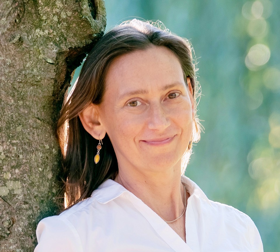 Headshot of Nadia Colburn, a light-skinned woman with long brown hair, next to a tree.