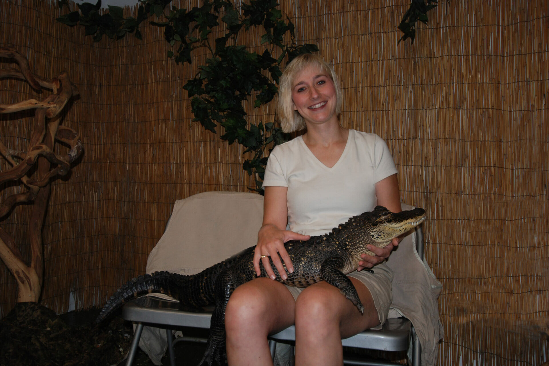 Joy Marzolf, a smiling white woman with blond hair, sits in a chair with an alligator sitting on her lap