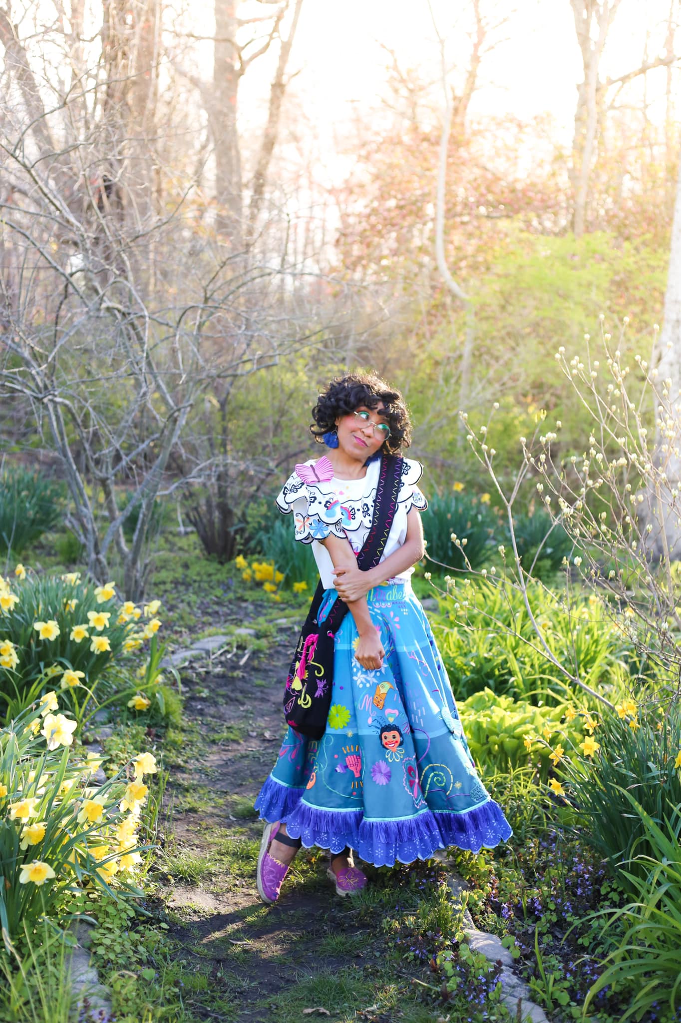 A Mirabel costumed performer, looking shy, stands outside surrounded by flowers and trees