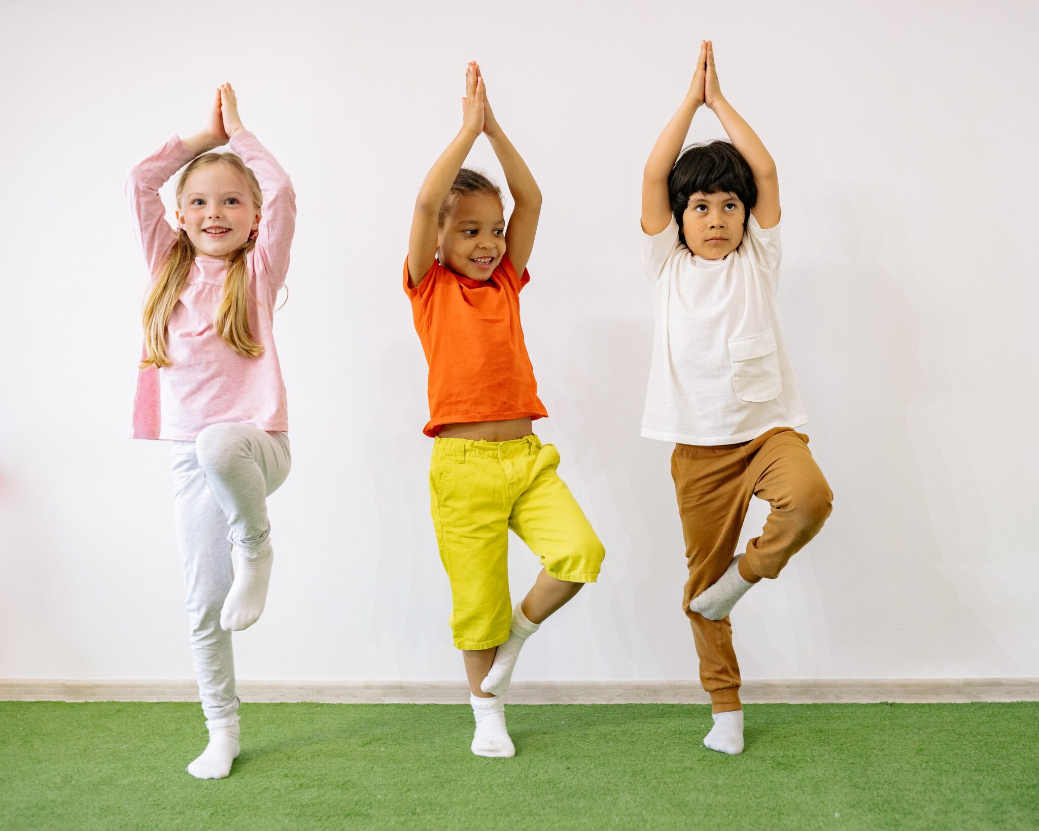 Three children standing in tree pose: hands above heads with palms together and one leg balanced against the other